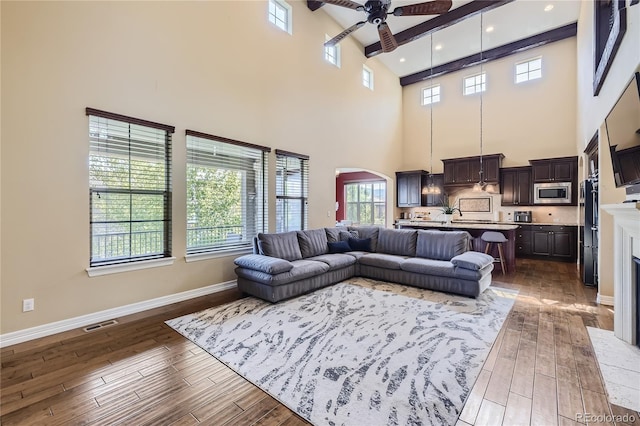 living room featuring a towering ceiling, beamed ceiling, dark hardwood / wood-style floors, and ceiling fan