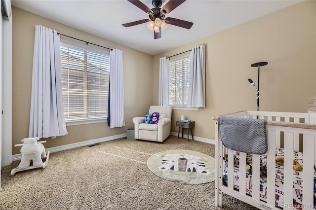 bedroom with ceiling fan, a nursery area, light colored carpet, and multiple windows