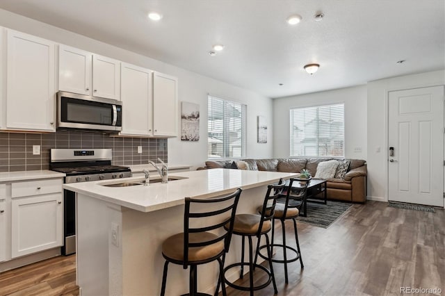 kitchen featuring a center island with sink, stainless steel appliances, decorative backsplash, open floor plan, and wood finished floors