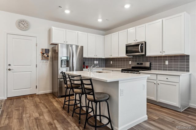 kitchen with wood finished floors, a sink, appliances with stainless steel finishes, an island with sink, and a kitchen bar