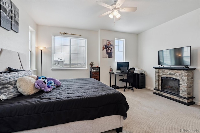 bedroom featuring ceiling fan, baseboards, carpet flooring, and a stone fireplace