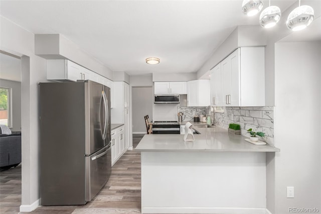 kitchen with tasteful backsplash, light wood-type flooring, kitchen peninsula, stainless steel appliances, and hanging light fixtures