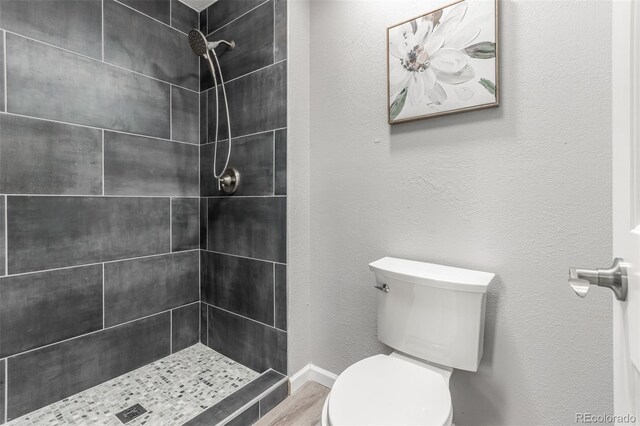 bathroom featuring hardwood / wood-style flooring, tiled shower, and toilet