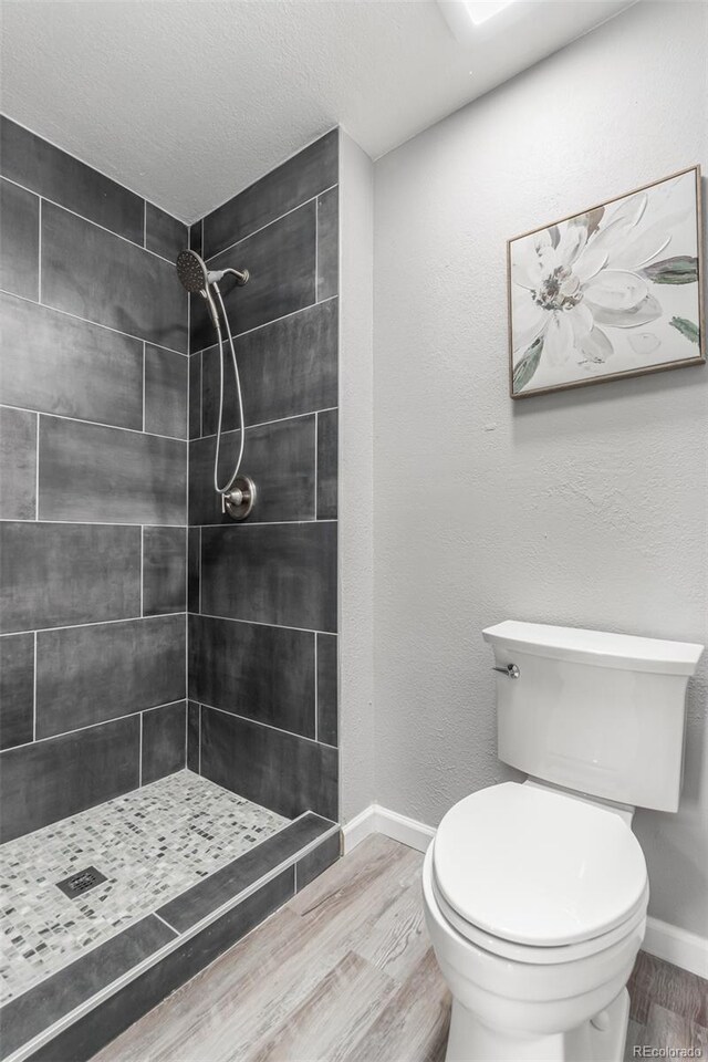 bathroom featuring a textured ceiling, toilet, a tile shower, and wood-type flooring