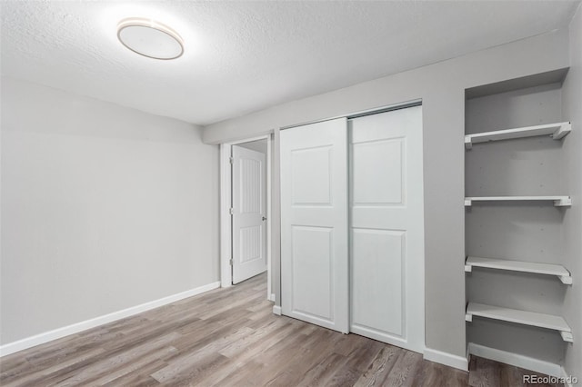 unfurnished bedroom with a textured ceiling, a closet, and light wood-type flooring