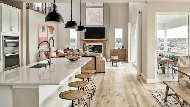 kitchen featuring sink, stainless steel double oven, hanging light fixtures, white cabinets, and light wood-type flooring