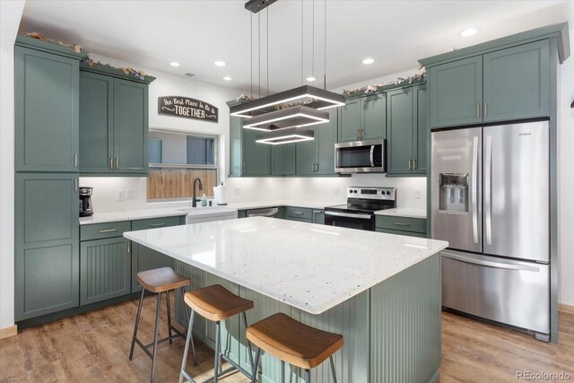 kitchen with a center island, sink, stainless steel appliances, light hardwood / wood-style flooring, and pendant lighting