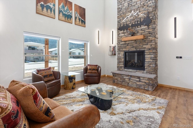 living room with a high ceiling, light hardwood / wood-style flooring, and a stone fireplace