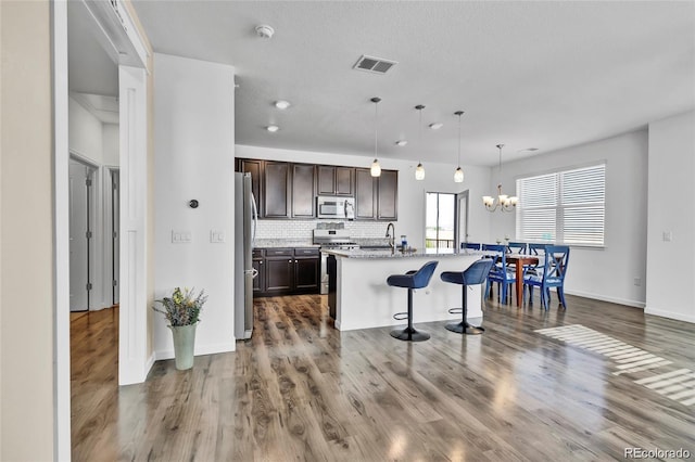 4569 Copeland Loop Unit 203, Highlands Ranch, CO 80126 - kitchen featuring appliances with stainless steel finishes, dark brown cabinets, wood finished floors, a kitchen breakfast bar, and tasteful backsplash