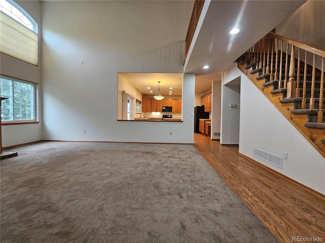 5571 S Sicily St, Aurora, CO 80015 - unfurnished living room featuring stairs, a high ceiling, wood finished floors, recessed lighting, and carpet floors