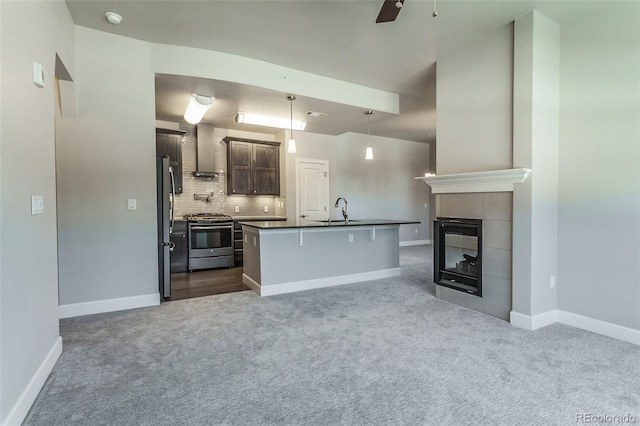 kitchen featuring a kitchen breakfast bar, wall chimney exhaust hood, stainless steel appliances, decorative light fixtures, and an island with sink