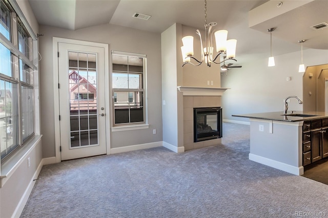 kitchen with pendant lighting, sink, vaulted ceiling, an island with sink, and a tiled fireplace