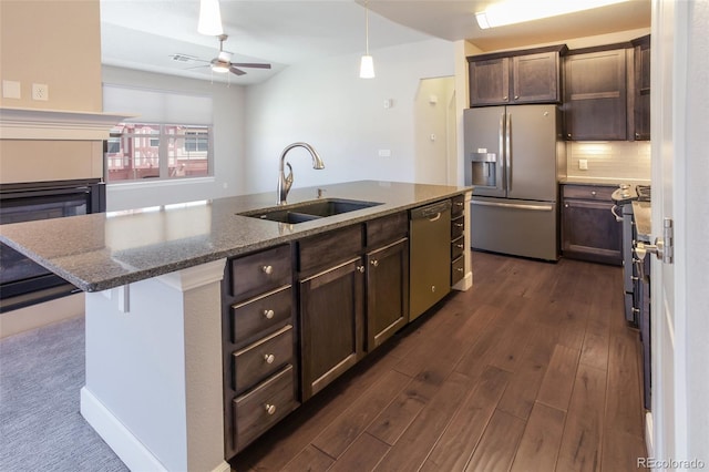 kitchen featuring dark stone counters, sink, an island with sink, appliances with stainless steel finishes, and dark brown cabinets