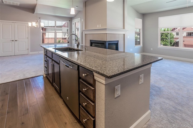 kitchen featuring dishwasher, sink, hanging light fixtures, light stone counters, and an island with sink