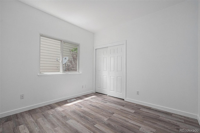 unfurnished bedroom featuring wood finished floors, baseboards, and a closet