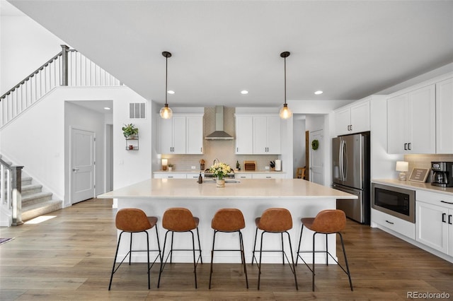 9016 Moondance Dr, Littleton, CO 80125 - kitchen featuring appliances with stainless steel finishes, wall chimney range hood, a breakfast bar, light countertops, and recessed lighting