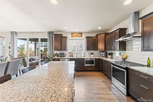 10091 Hannaway Dr, Colorado Springs, CO 80924 - kitchen featuring stainless steel appliances, wall chimney exhaust hood, healthy amount of natural light, dark brown cabinetry, and recessed lighting