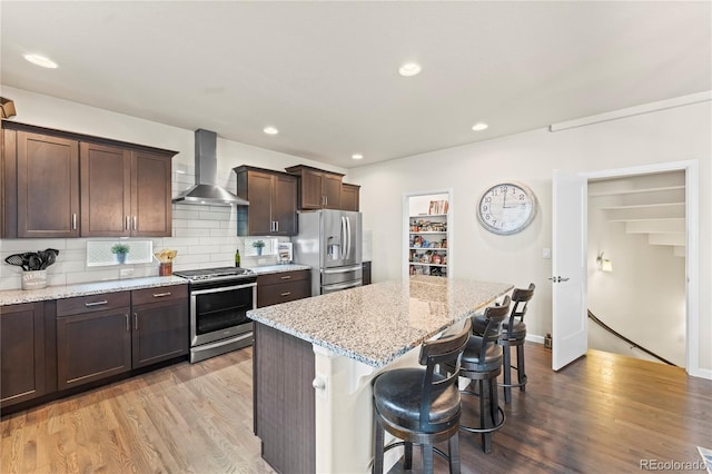 10091 Hannaway Dr, Colorado Springs, CO 80924 - kitchen featuring wall chimney exhaust hood, appliances with stainless steel finishes, a breakfast bar area, a center island, and dark brown cabinetry