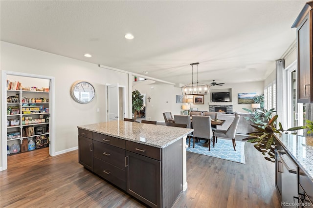 10091 Hannaway Dr, Colorado Springs, CO 80924 - kitchen with dark wood-type flooring, a kitchen island, open floor plan, a stone fireplace, and recessed lighting