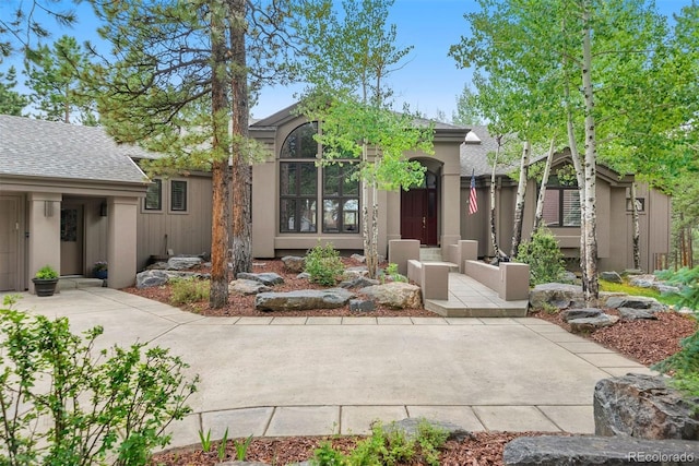 view of front facade featuring stucco siding, a shingled roof, and a patio area