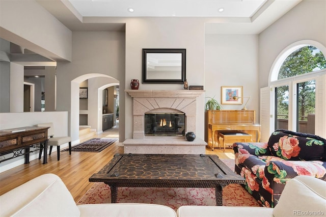 living room with wood finished floors, a premium fireplace, recessed lighting, arched walkways, and a towering ceiling