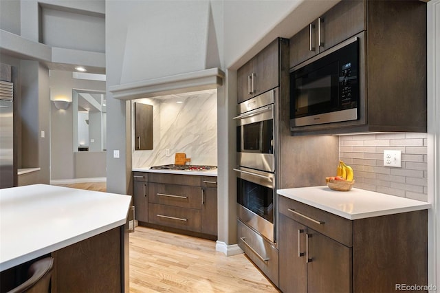 kitchen featuring light wood-type flooring, light countertops, dark brown cabinets, built in appliances, and tasteful backsplash