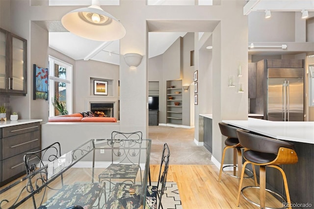 dining space with light wood finished floors, track lighting, baseboards, and a lit fireplace