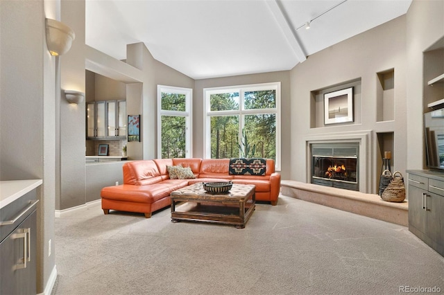 carpeted living room featuring a glass covered fireplace, vaulted ceiling, and track lighting