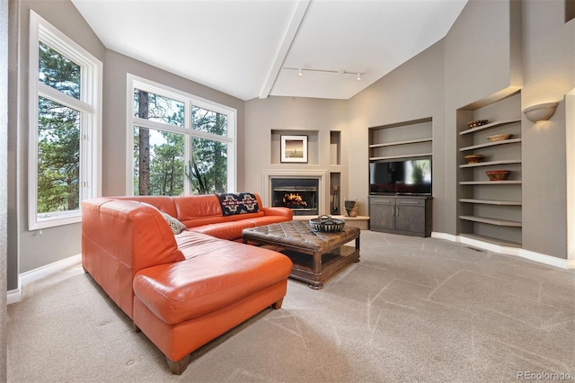 living area with built in shelves, baseboards, a warm lit fireplace, track lighting, and light colored carpet