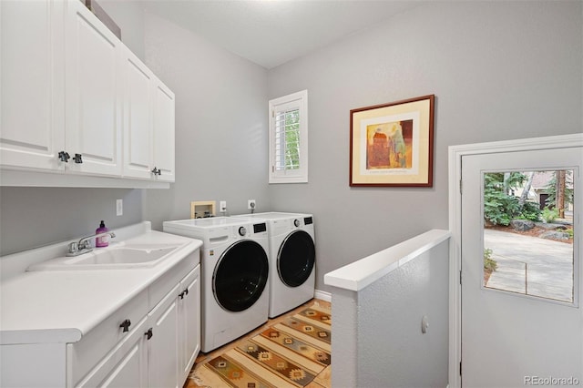 clothes washing area featuring a sink, cabinet space, light wood-style flooring, and washing machine and clothes dryer