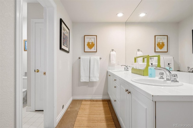 bathroom featuring double vanity, toilet, baseboards, and a sink