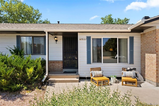 property entrance featuring a shingled roof and brick siding