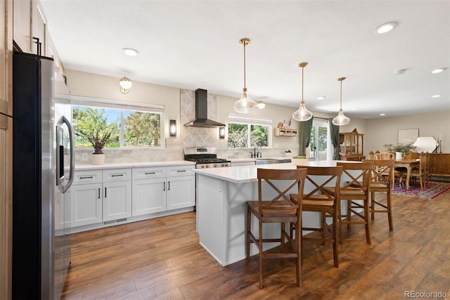 kitchen featuring stainless steel appliances, white cabinets, hanging light fixtures, light countertops, and wall chimney exhaust hood