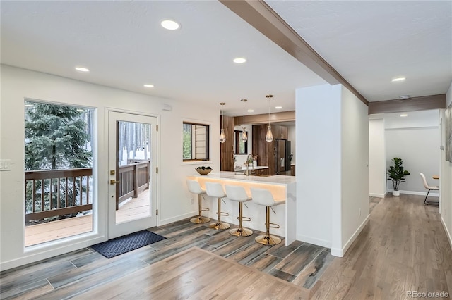 kitchen with hanging light fixtures, refrigerator with ice dispenser, a kitchen breakfast bar, wood finished floors, and baseboards