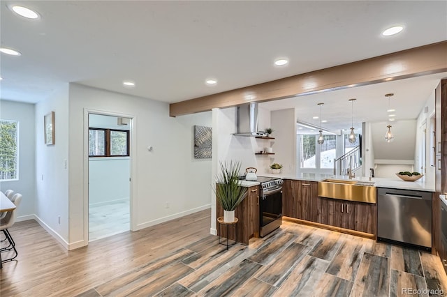 kitchen with light countertops, appliances with stainless steel finishes, a sink, modern cabinets, and wall chimney exhaust hood