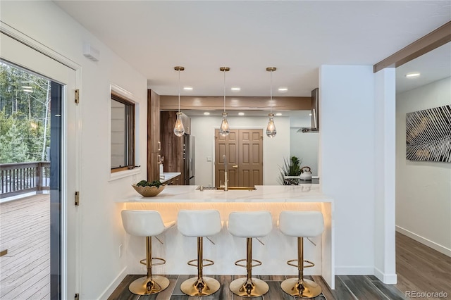 kitchen with baseboards, a breakfast bar area, dark wood-type flooring, freestanding refrigerator, and a sink