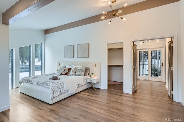 bedroom with light wood finished floors, baseboards, lofted ceiling, a walk in closet, and a notable chandelier