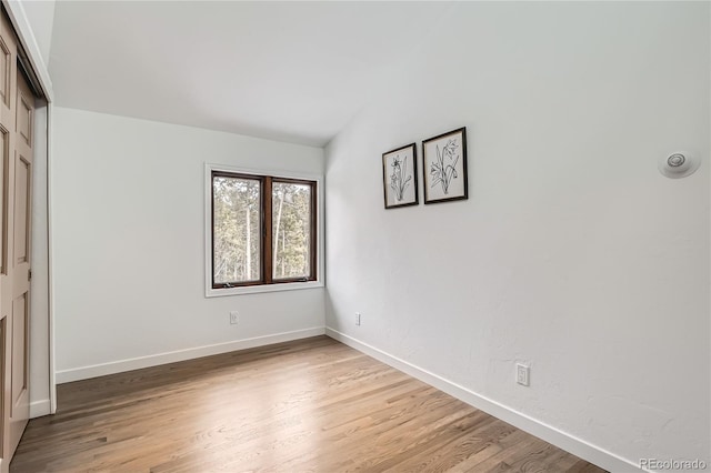 unfurnished bedroom with light wood-type flooring, a closet, lofted ceiling, and baseboards