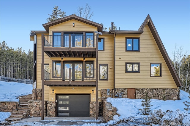 view of front of house with a garage, stone siding, and a balcony