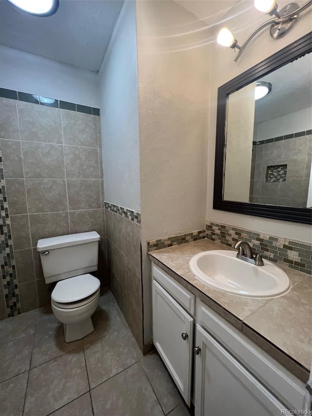 bathroom with tile flooring, tile walls, backsplash, toilet, and vanity with extensive cabinet space