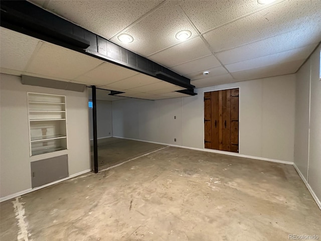 basement featuring a drop ceiling and built in shelves