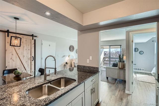 499 Wright St Unit 308, Lakewood, CO 80228 - kitchen featuring visible vents, a barn door, dark stone countertops, a sink, and light wood finished floors