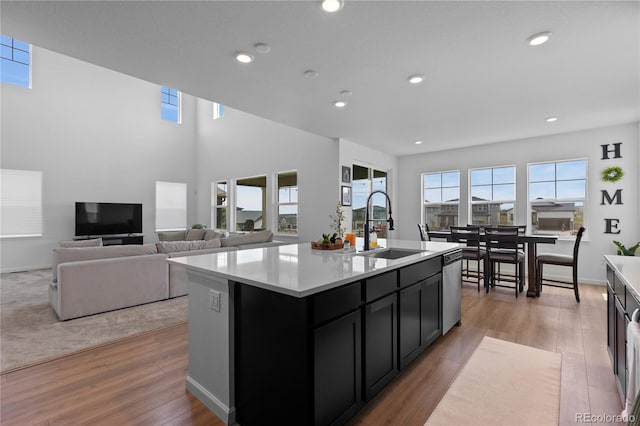 8550 Cheraw St, Littleton, CO 80125 - kitchen with dark cabinetry, light wood-style floors, light countertops, stainless steel dishwasher, and a center island with sink