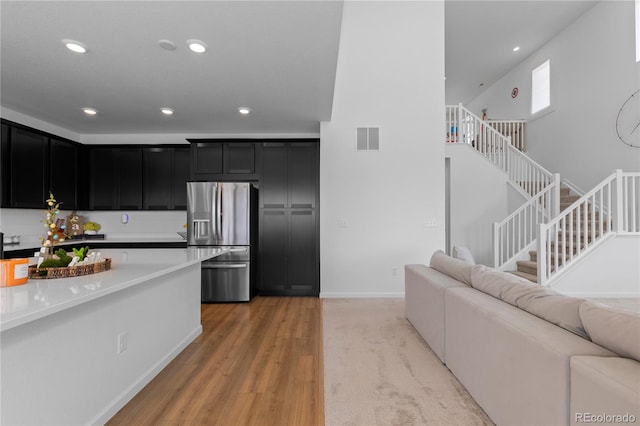 8550 Cheraw St, Littleton, CO 80125 - kitchen featuring stainless steel fridge with ice dispenser, dark cabinetry, recessed lighting, open floor plan, and light wood-style floors