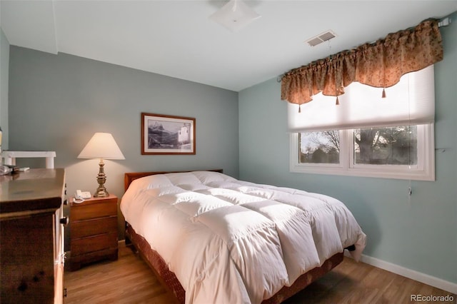 bedroom with visible vents, baseboards, and wood finished floors