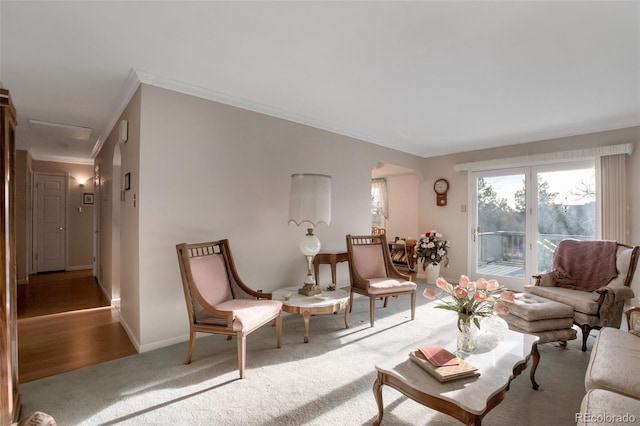 carpeted living area featuring baseboards, arched walkways, and crown molding