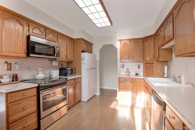 kitchen with a sink, light countertops, light wood-style floors, appliances with stainless steel finishes, and backsplash