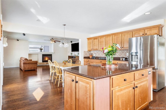 kitchen with a center island, dark hardwood / wood-style flooring, dark stone countertops, decorative backsplash, and stainless steel fridge with ice dispenser