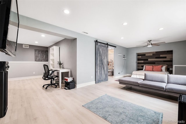 living room with ceiling fan, a barn door, and light wood-type flooring