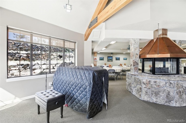 carpeted living room featuring beam ceiling, high vaulted ceiling, ceiling fan, and a stone fireplace